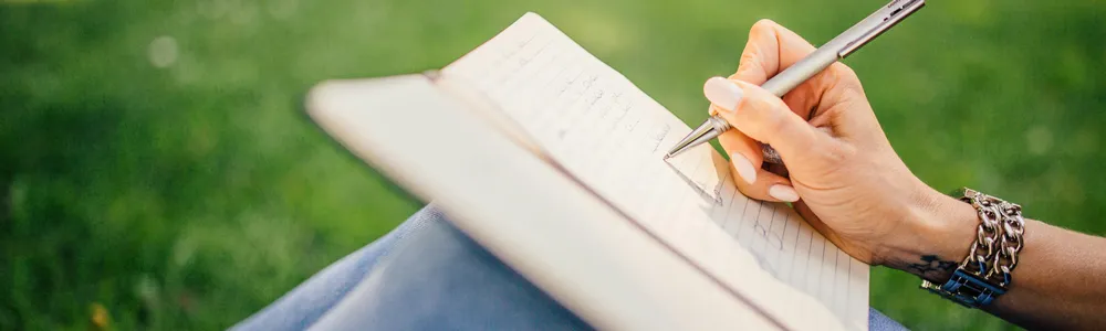 Donna seduta sul prato, scrive sul diario posato sulle ginocchia