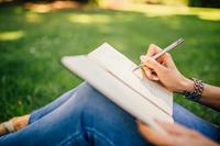 Donna seduta sul prato, scrive sul diario posato sulle ginocchia