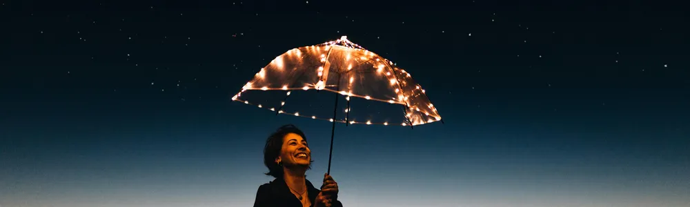Donna felice al tramonto sotto un ombrello con lucine led