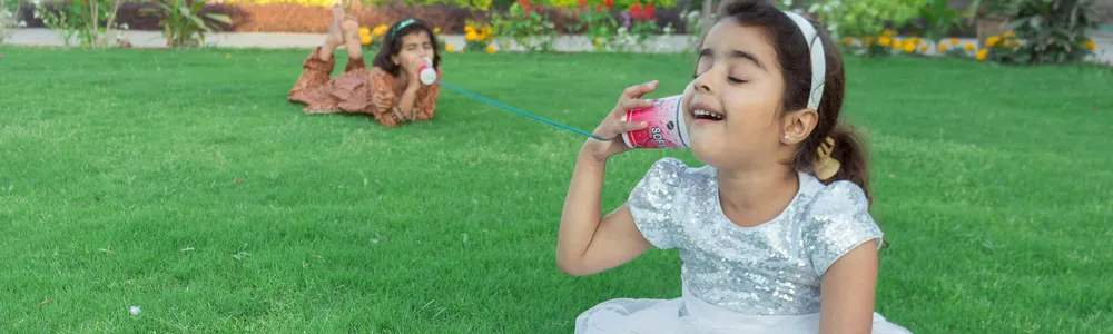 Bambine sul prato una che parla in un barattolo mentre l'altra ascolta in un altro barattolo collegati da un filo