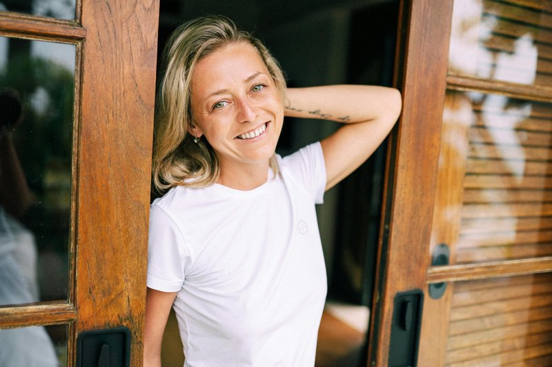 Donna bionda appoggiata alla porta che sorride toccandosi i capelli