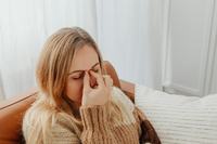 Donna seduta sul divano vicino alla finestra con gli occhi chiusi e la mano sulla radice del naso
