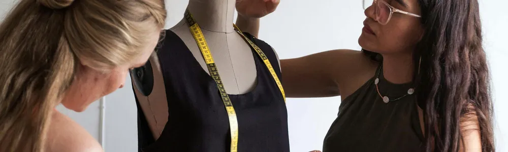 due ragazze attorno ad un manichino prendono le misure dell'abito